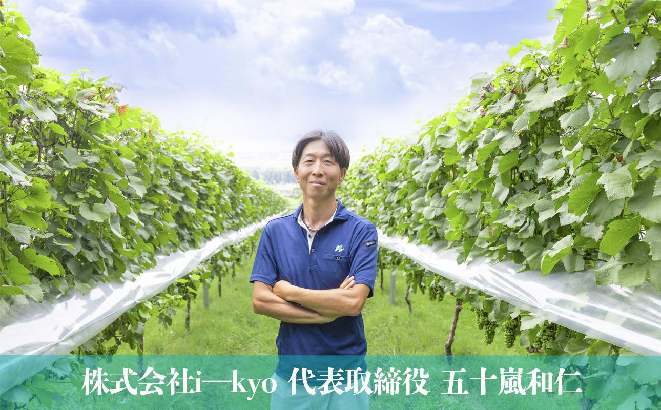 水沢の広大なぶどう畑を背にするi-kyo代表・五十嵐和仁氏る