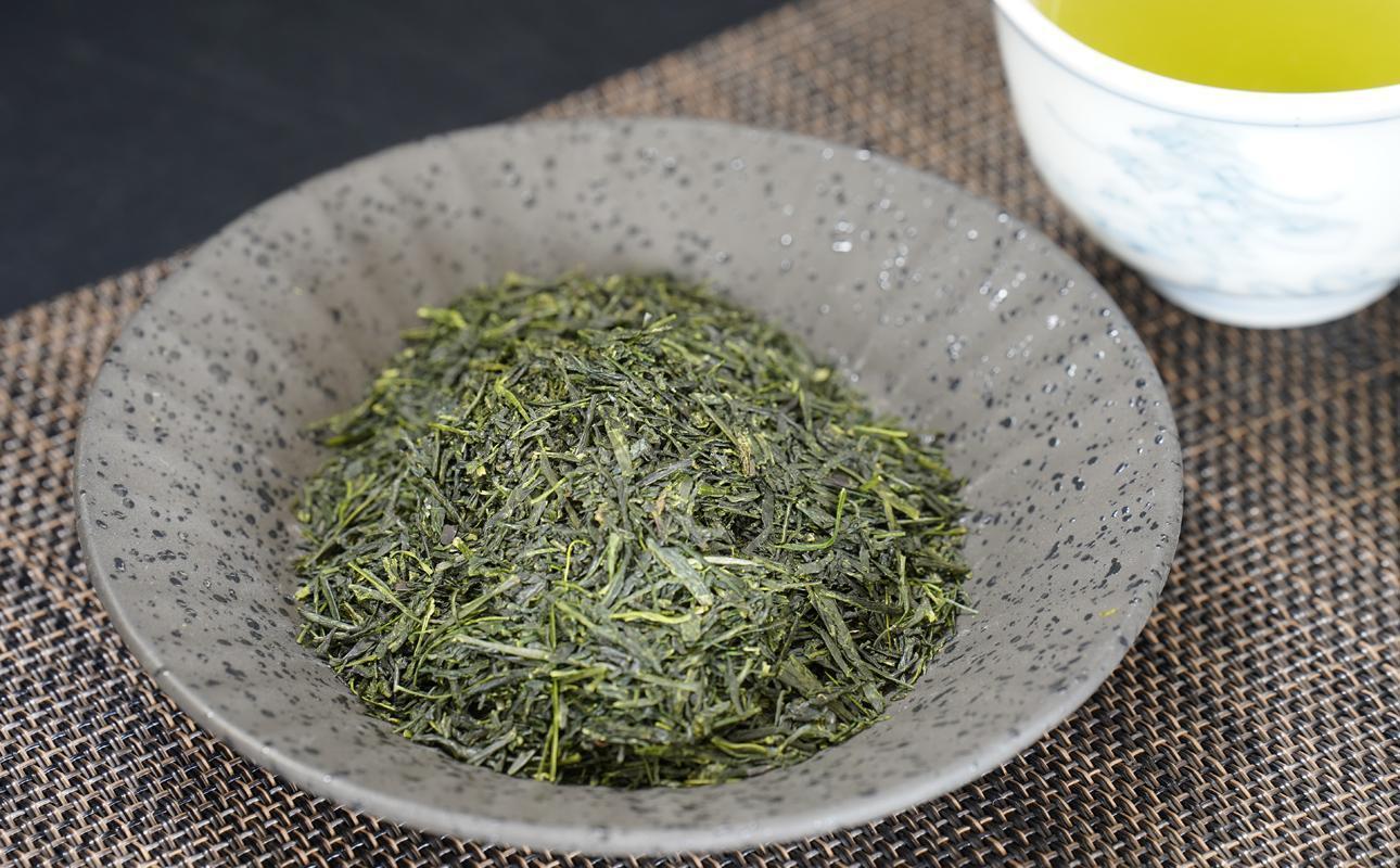 灰色の斑点の器に盛られた緑色の茶葉と湯のみ。